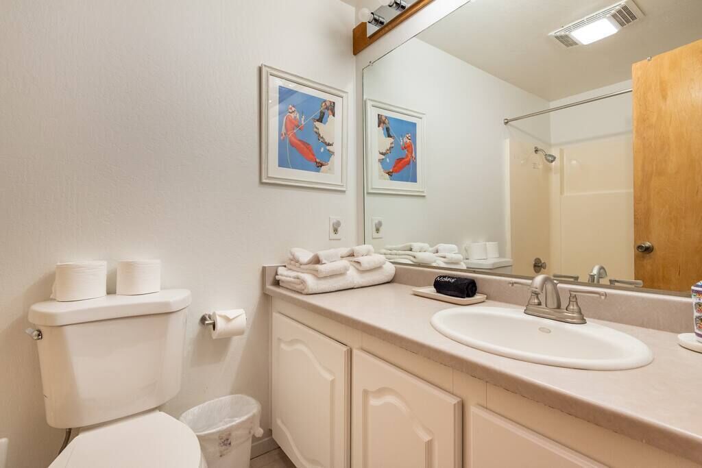 A bathroom with a toilet, sink, mirror, and framed artwork on the wall.