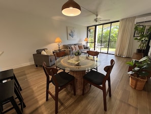 Un vaste espace de vie comprenant une table ronde en verre, plusieurs chaises, un ensemble de canapés et un ventilateur de plafond.