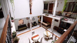 Ein mehrgeschossiges Atrium mit einem hölzernen Kruzifix, Zimmerpflanzen und einem Essbereich mit Stühlen und Tischen.