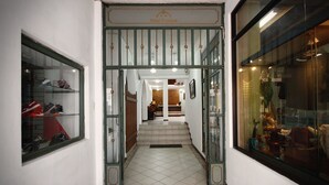 Ein Hotel Eingang mit gefliestem Boden, einer Holztreppe und einer Glastür mit Metallrahmen.