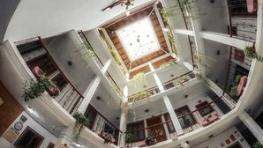 Ein mehrgeschossiges Atrium mit einem zentralen offenen Bereich, mehreren Balkonen und Topfpflanzen.