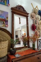 A mirror with a wooden frame, a wall with hats, a woven basket, and a potted plant.