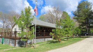 A building with a porch and a flagpole, surrounded by trees and a gravel path.