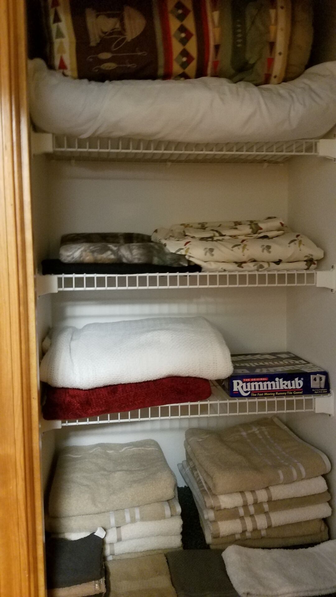 A closet with shelves holding folded towels and a board game.