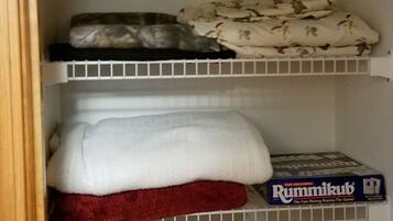 A closet with shelves holding folded towels and a board game.