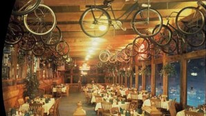 A restaurant with wooden interiors, bicycles hanging from the ceiling, and tables set for dining.