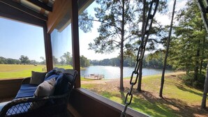 Una habitación con vistas a un lago, una silla de mimbre con cojines y una taza de café sobre una mesa.