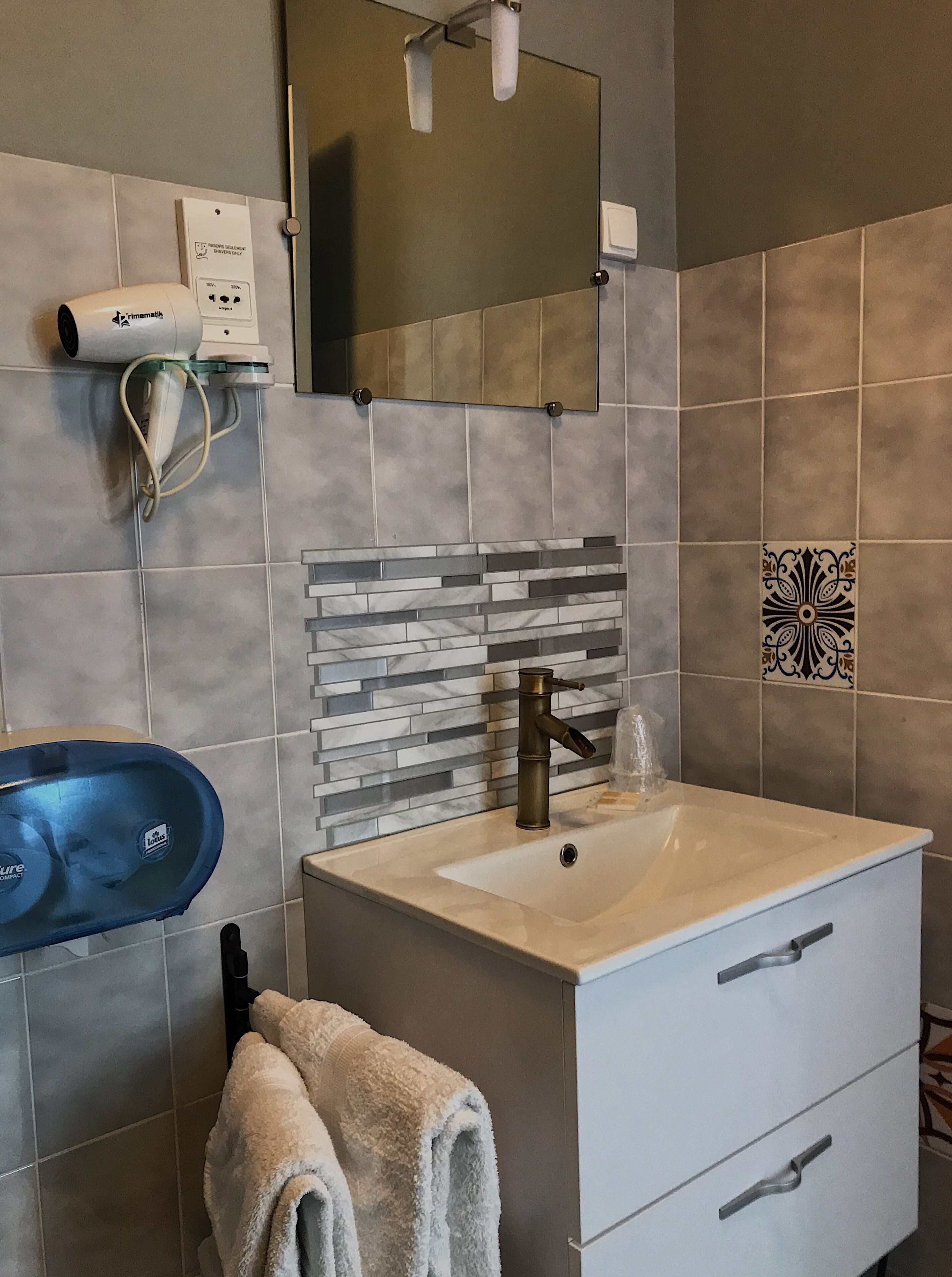 A bathroom with a white sink, a towel rack, a mirror, and a hairdryer on the wall.