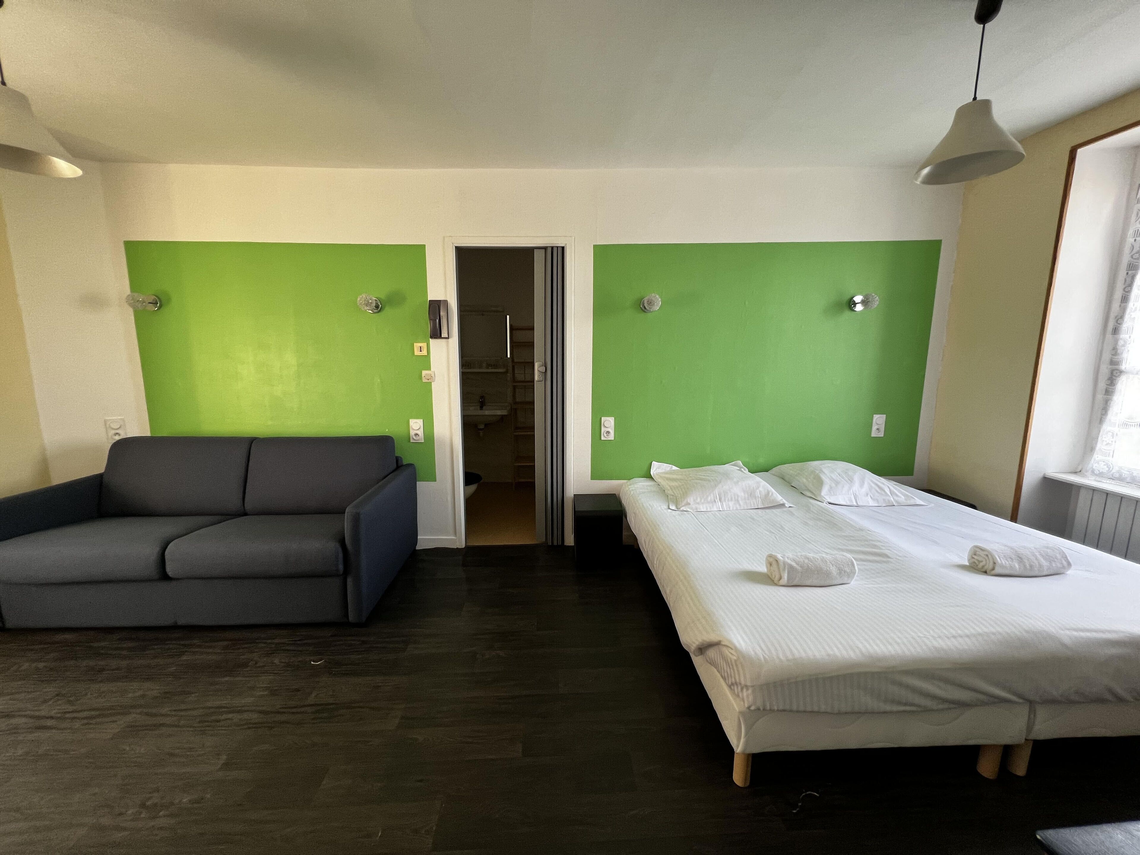 Une pièce comprenant un lit, un canapé et une salle de bain, visible à travers une porte ouverte.