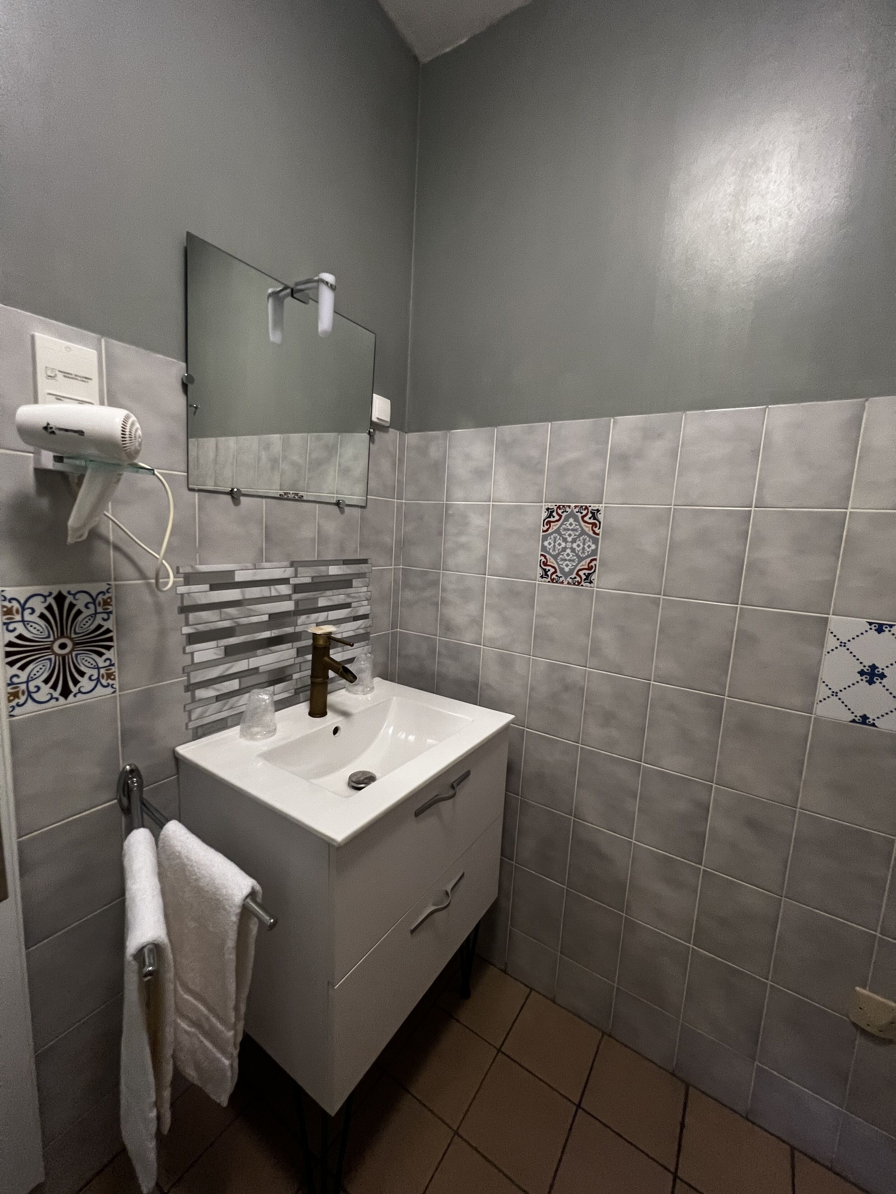 Un baño con lavamanos blanco, espejo y toallero.