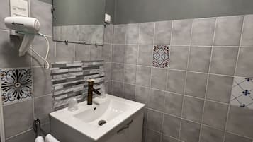 Un baño con lavamanos blanco, espejo y toallero.