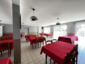 Un comedor amplio con varias mesas y sillas, ventanas grandes y un techo alto.