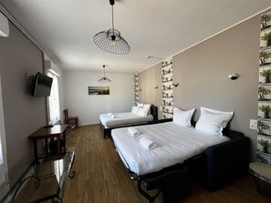 Habitación de hotel con dos camas, un escritorio, una silla, un televisor y una pared con cuadros.
