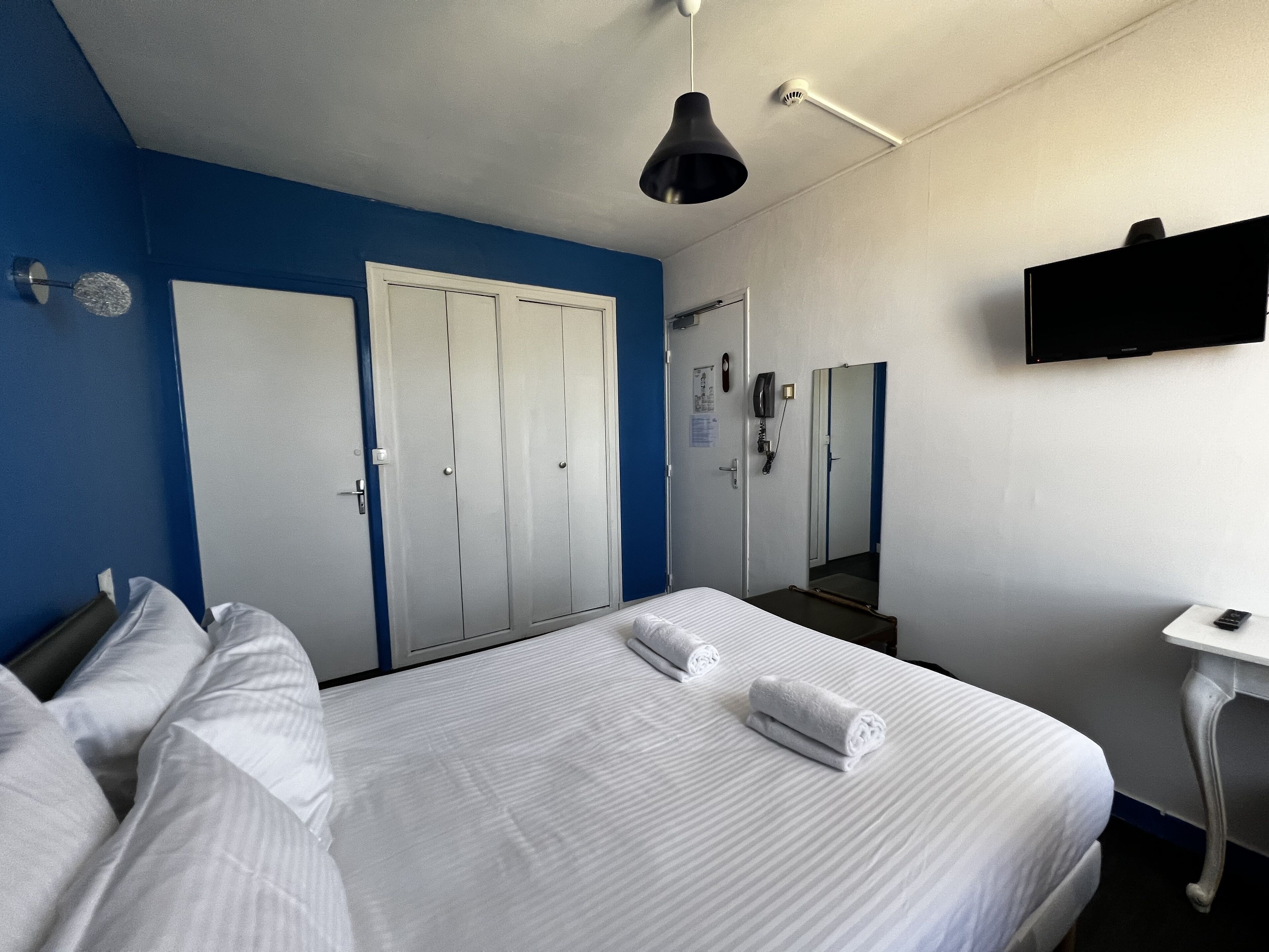 Una habitación de hotel con cama, escritorio, espejo, televisor y armario.
