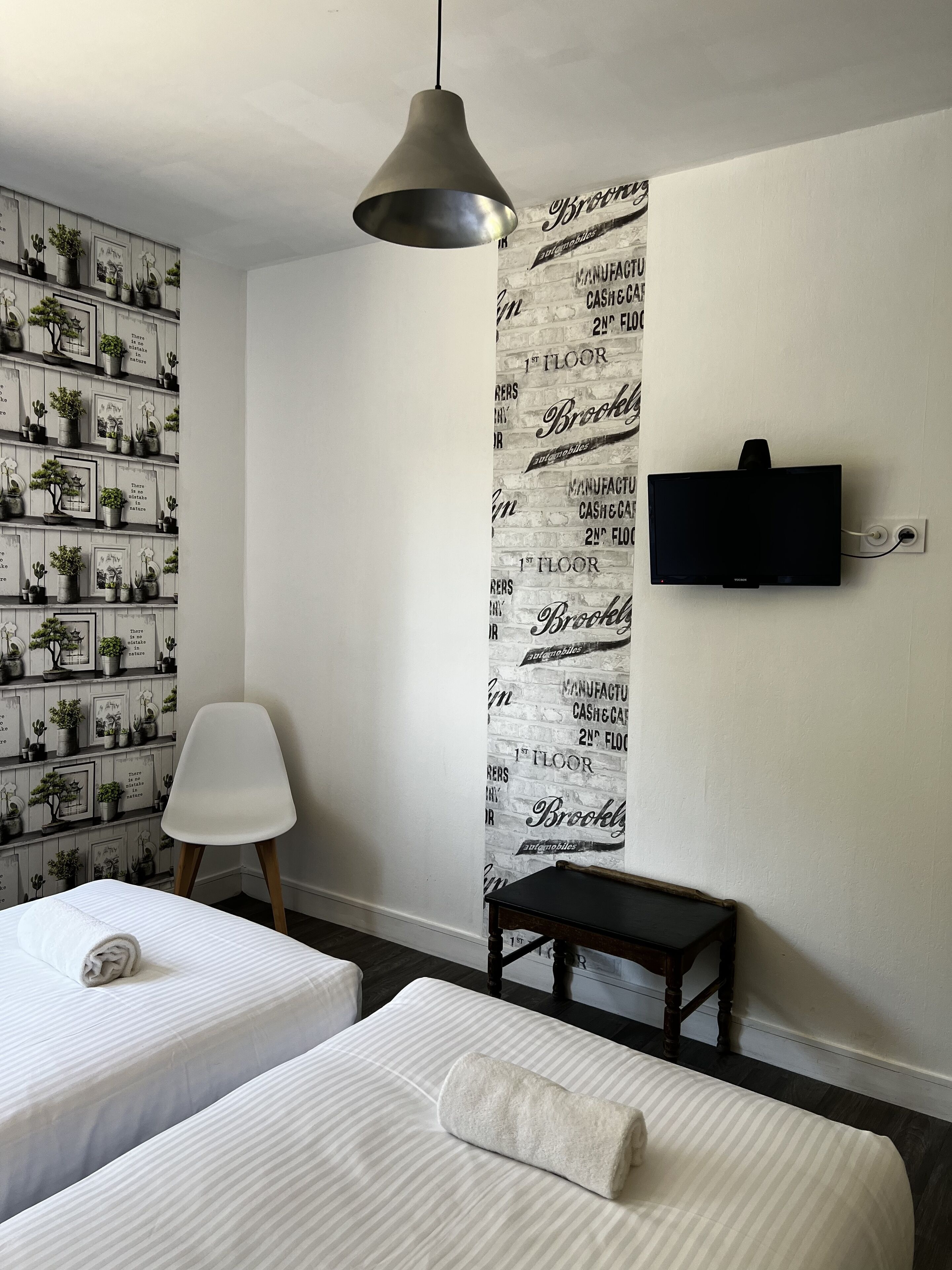 Ein Hotelzimmer mit zwei Betten, einem Wandfernseher, einem kleinen Tisch und einem Sessel.