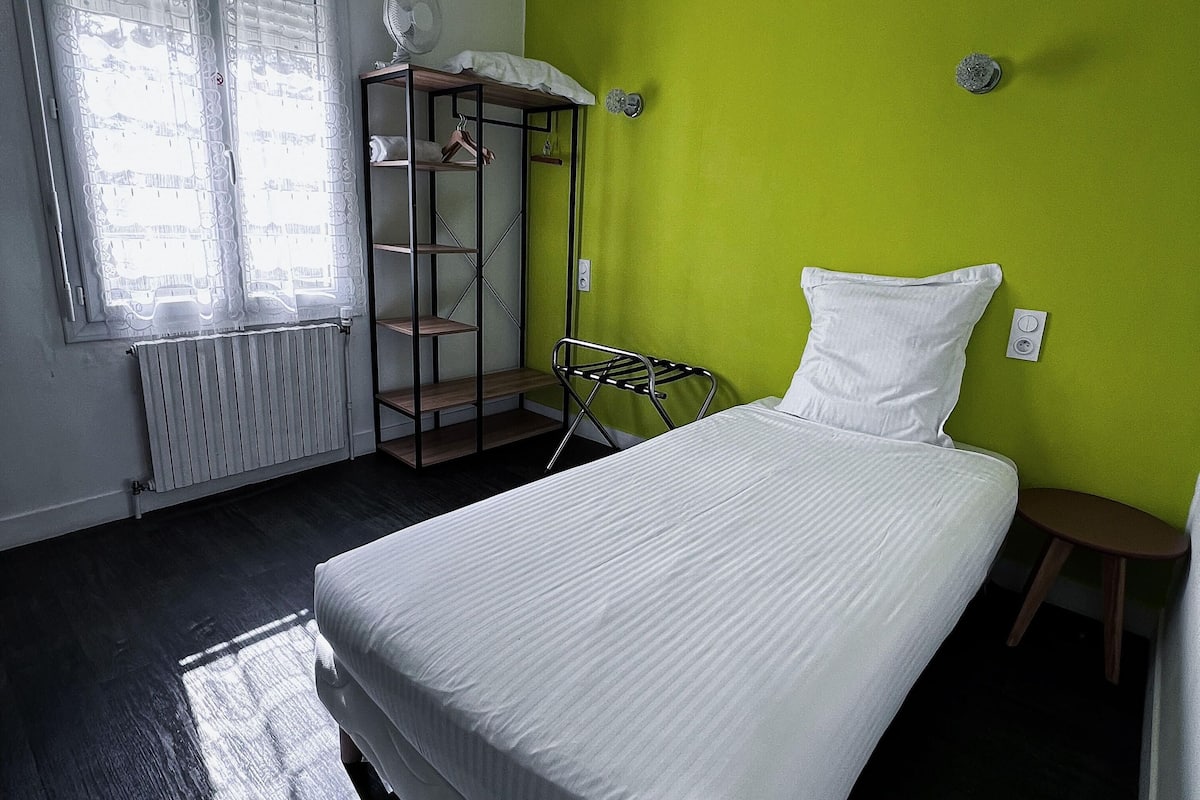 A bedroom with a bed, a radiator, a green wall, and a window with blinds.