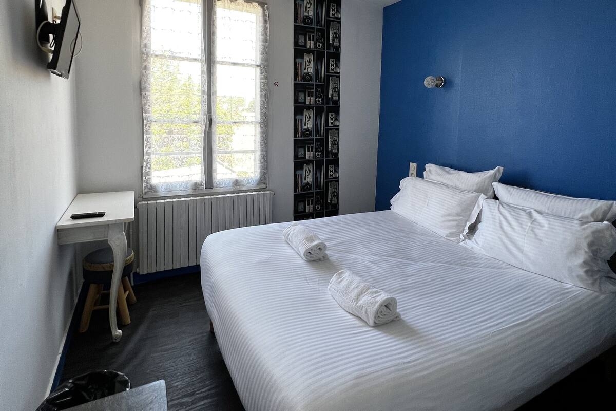A bedroom with a large bed, a desk, a radiator, and a window with curtains.