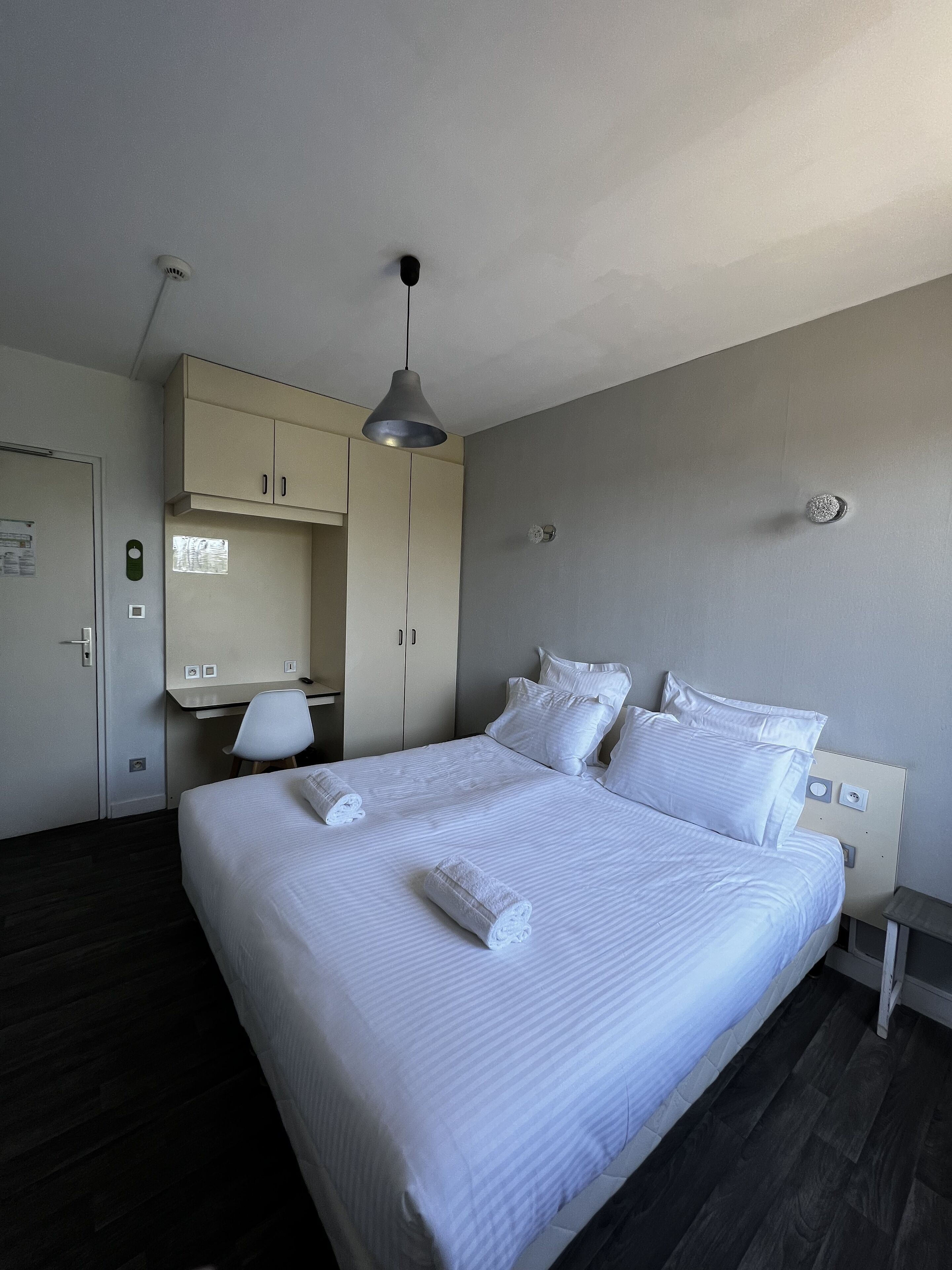 A hotel room with a bed, a desk, a chair, and a wardrobe.