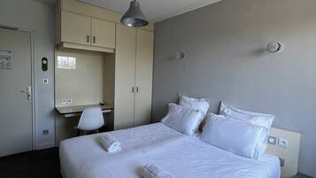 A hotel room with a bed, a desk, a chair, and a wardrobe.