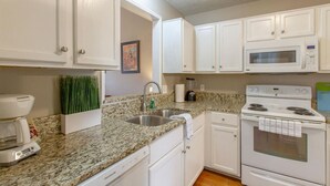 A kitchen with white cabinets, a granite countertop, a stainless steel sink, a coffee maker, a microwave, and a stove. - Bright & Fresh - Large Backyard - Mins to Broadway (Nashville)