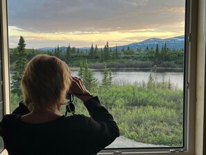 Una persona tomando una foto a través de una ventana con vistas a un paisaje natural con montañas y un lago.