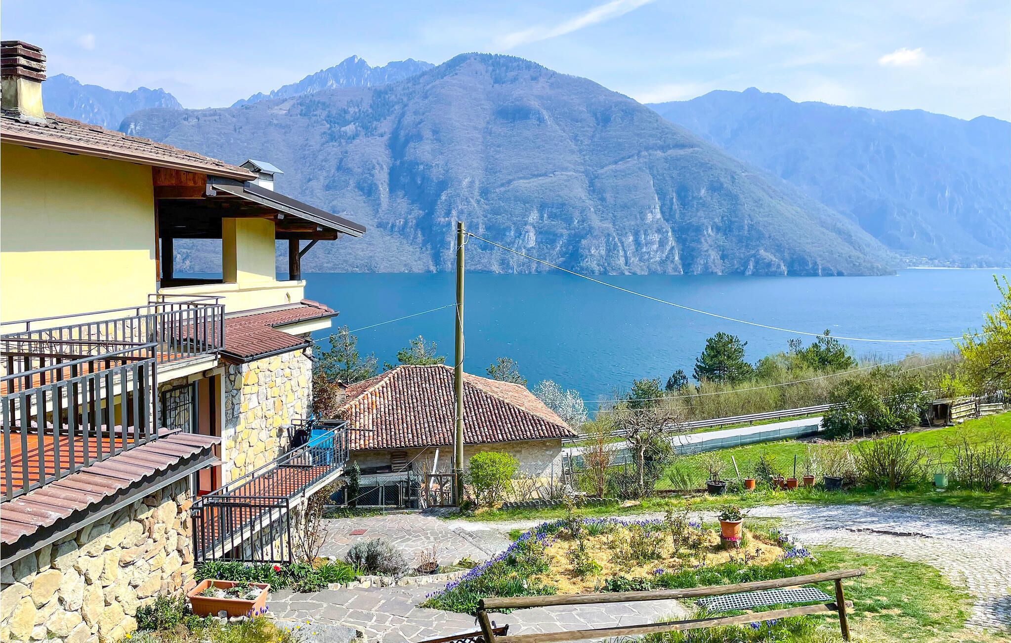 A mountain house with a stone facade, a balcony, and a view of a lake and mountains.