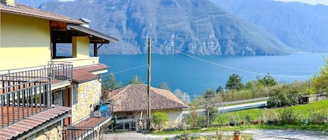 Ett hus beläget i bergen med en fasad av sten, en balkong och utsikt över en sjö och berg.
