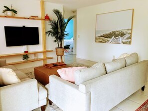 A living room with a sofa, a coffee table, a TV mounted on the wall, and a potted plant. - 3 Bedroom 2 Bath House with pool - Close to the beach and downtown (Stuart)