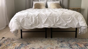 A neatly made bed with a white duvet, two fluffy pillows, and a patterned rug on a tiled floor.