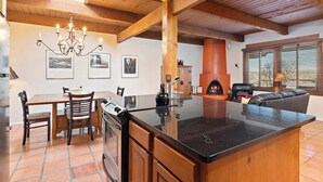 A kitchen with a central island, wooden beams, a chandelier, and a dining area with chairs and a table. - Fort Marcy 06 | Walk to Plaza | Kiva Fireplace | Full Kitchen | Hot Tub | Pool | Single Level (Santa Fe)