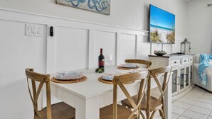 A dining area with a white table, four wooden chairs, a bottle of wine, and a painting of an octopus.