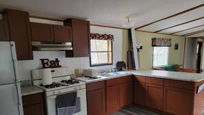 Une cuisine avec des meubles de rangement en bois, un fourneau blanc et une fenêtre avec des rideaux.