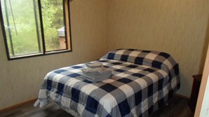 Une chambre avec une couvre-lit à carreaux, une fenêtre donnant sur un paysage verdoyant et un plancher en bois.
