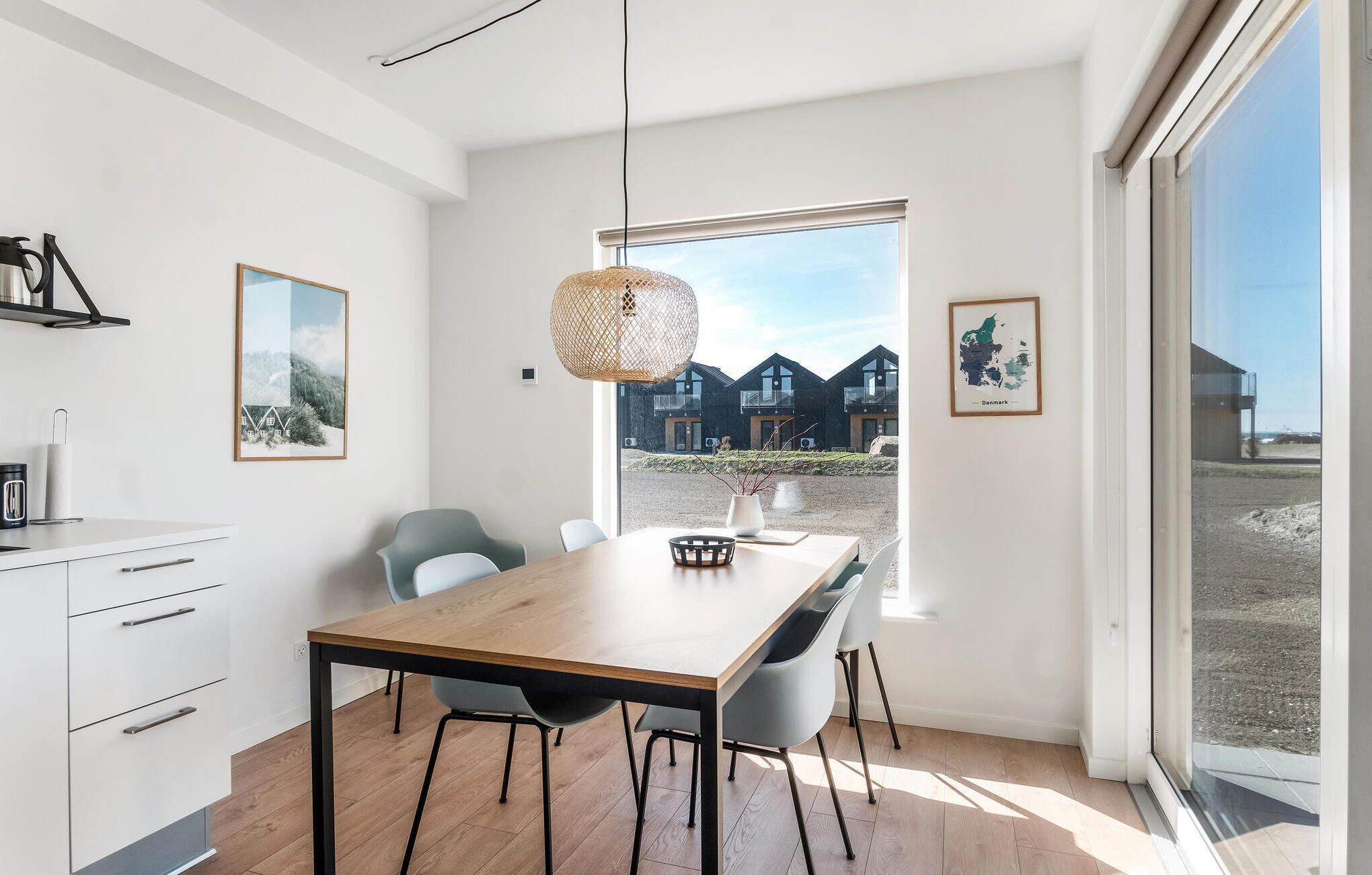 Une cuisine moderne avec une table et des chaises en bois, un luminaire suspendu et une vue sur un immeuble doté de nombreux balcons.