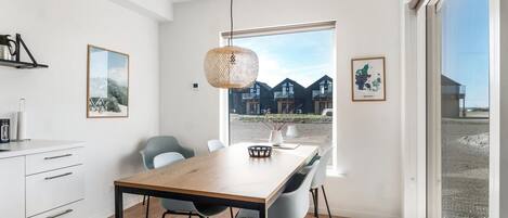 Une cuisine moderne avec une table et des chaises en bois, un luminaire suspendu et une vue sur un immeuble doté de nombreux balcons.