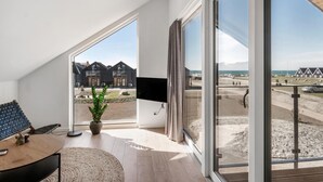 A modern room with a large sliding glass door leading to a beach view, a flat-screen TV mounted on the wall, and a cozy seating area with a table and chairs. - Stunning apartment in Slagelse (Slagelse)