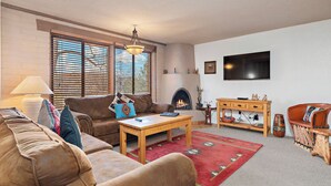 Una sala de estar con chimenea, televisor montado en la pared, sofá, mesa de centro y alfombra.