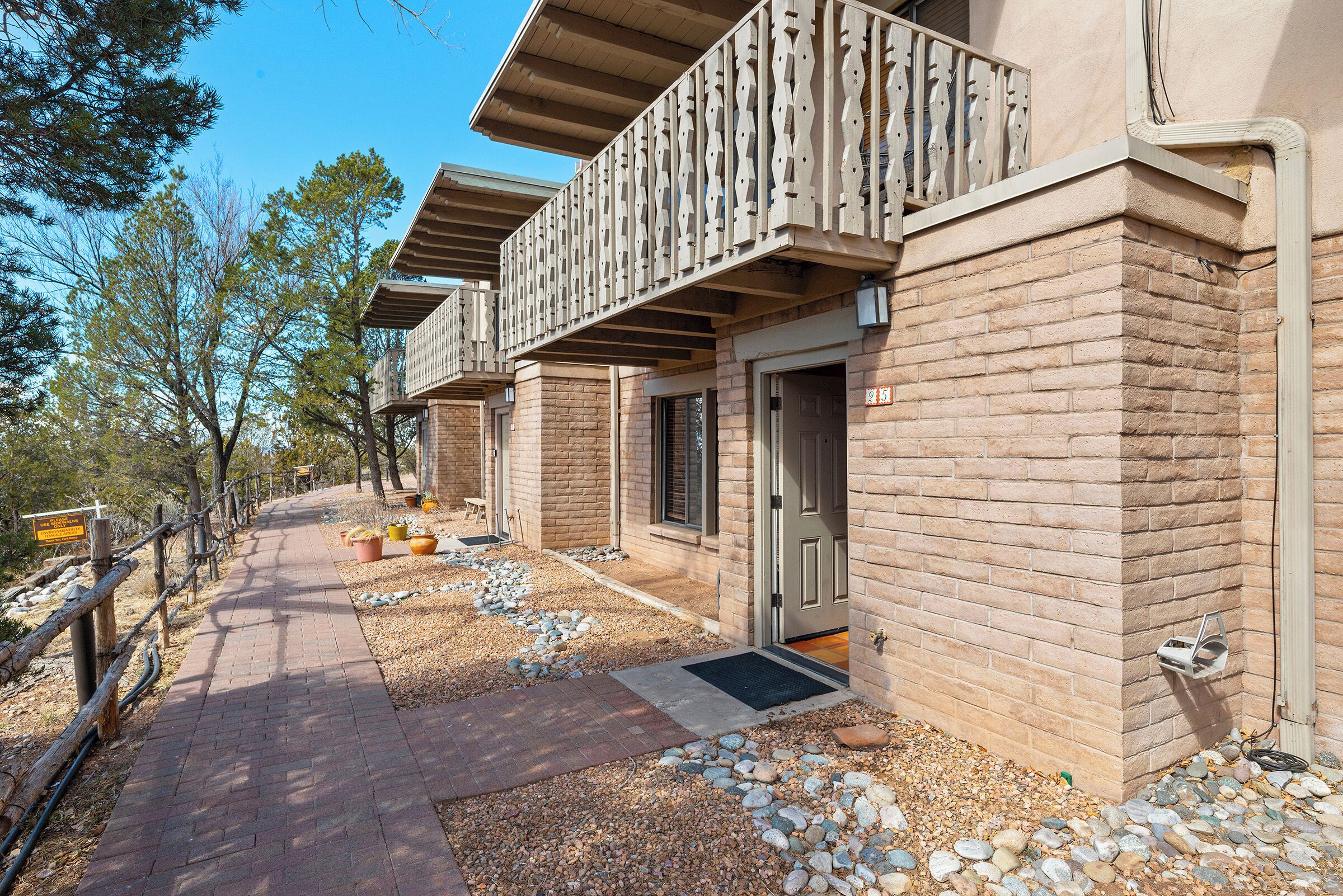 A row of brick buildings with balconies, a paved walkway, and a gravel area with potted plants.