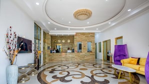 A hotel lobby with a reception desk, a large chandelier, and a purple sofa. - Reno Apartments Abuja (Abuja)
