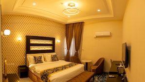 A hotel room with a large bed, a desk, a chair, a TV, and a coffee maker. - Reno Apartments Abuja (Abuja)