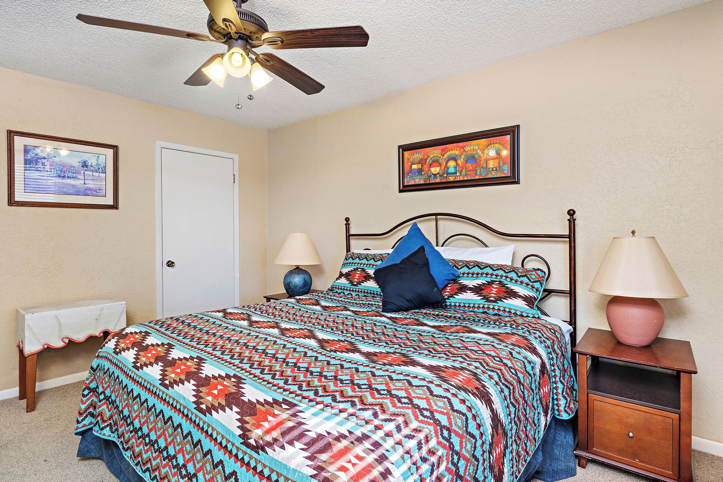 A bedroom with a bed, a nightstand, a dresser, a ceiling fan, and two framed pictures on the wall.