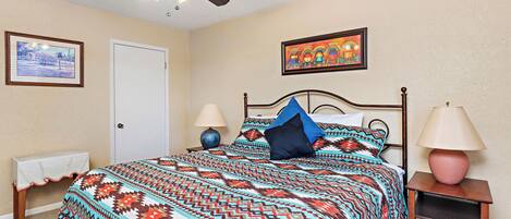 A bedroom with a bed, a nightstand, a dresser, a ceiling fan, and two framed pictures on the wall.