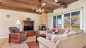 A living room with a fireplace, a sofa, a TV, and a wooden ceiling. - Fort Marcy 28 | Walk to Plaza | Fireplace | Kitchen | Hot Tub | Pool | End Unit | Single Level (Santa Fe)