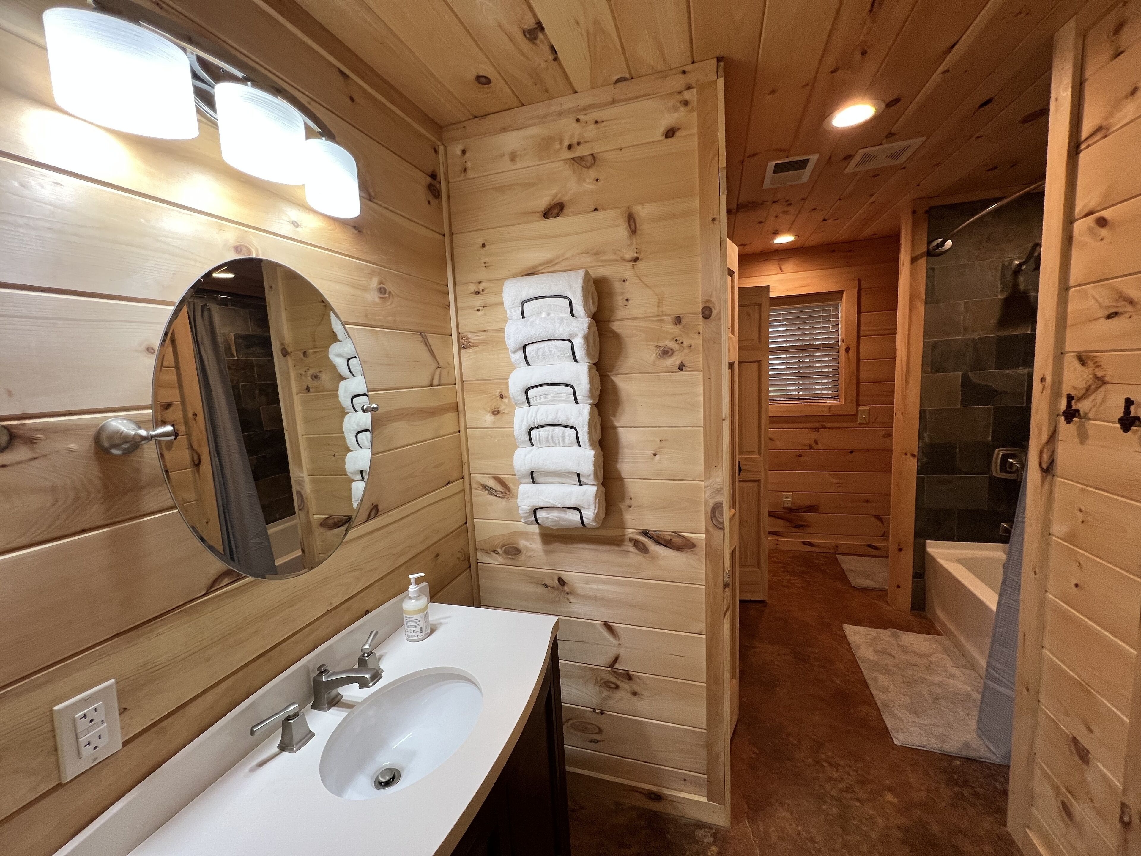 Une salle de bain rustique, aménagée dans une cabane en bois, avec un lavabo, un miroir, un porte-serviettes et une douche.