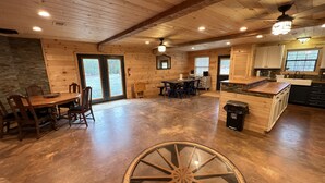 Un intérieur de chalet en bois spacieux, comprenant un coin repas, une cuisine et de grandes fenêtres.