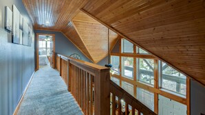 Una escalera de madera que lleva a un dormitorio estilo altillo con un ventanal grande.