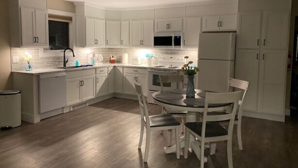 Een moderne keuken met witte kasten, een eethoek met een ronde tafel en stoelen, en een ingebouwde magnetron boven het aanrecht.