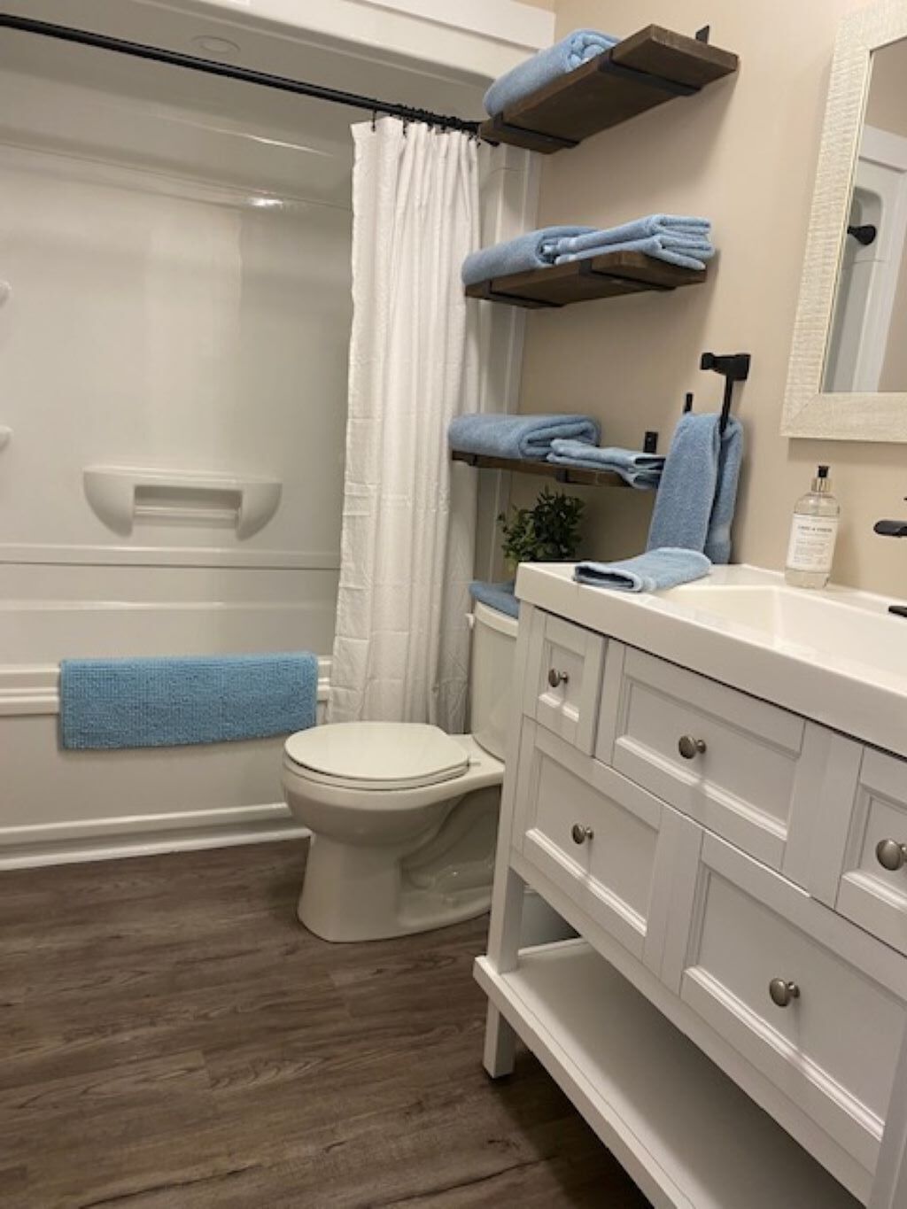 A bathroom with a toilet, a sink with a mirror, a towel rack with towels, and a shower curtain.