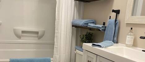 A bathroom with a toilet, a sink with a mirror, a towel rack with towels, and a shower curtain.