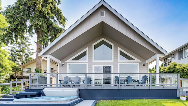 Una casa moderna con una terraza amplia, bañera de hidromasaje al aire libre y un césped bien cuidado.